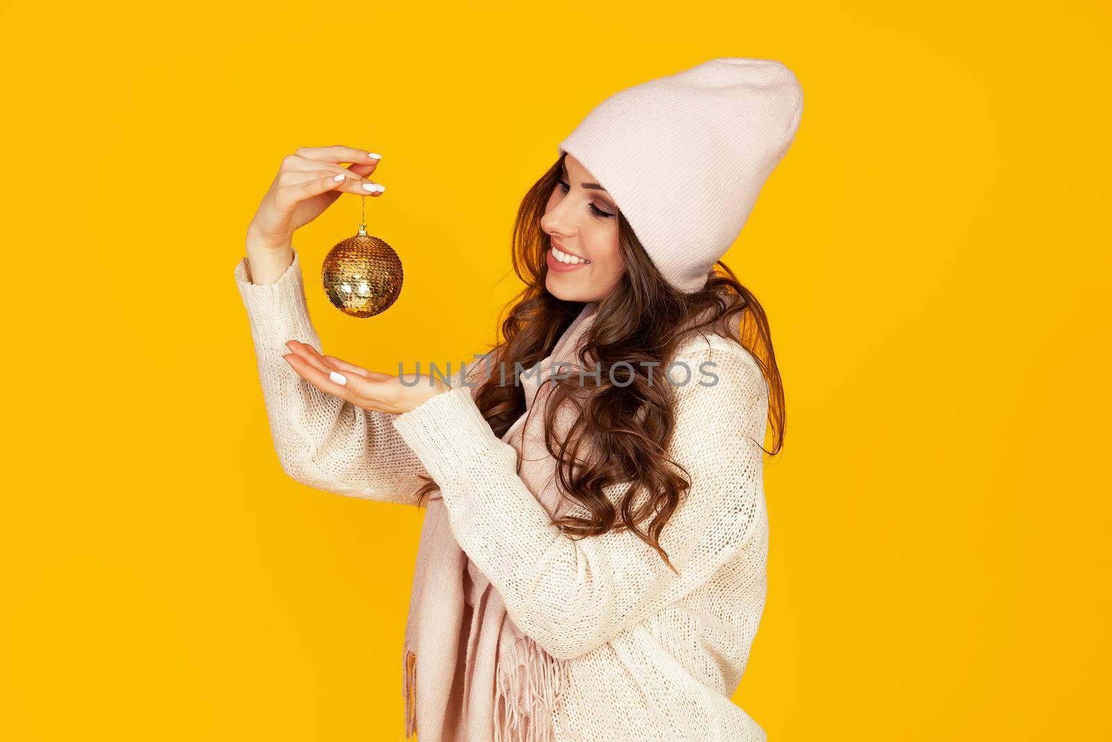 Happy young smiling woman holding a christmas tree ball promoting a best offer christmas tree. A girl in a sweater looks at a Christmas tree toy. New year and christmas holiday concept