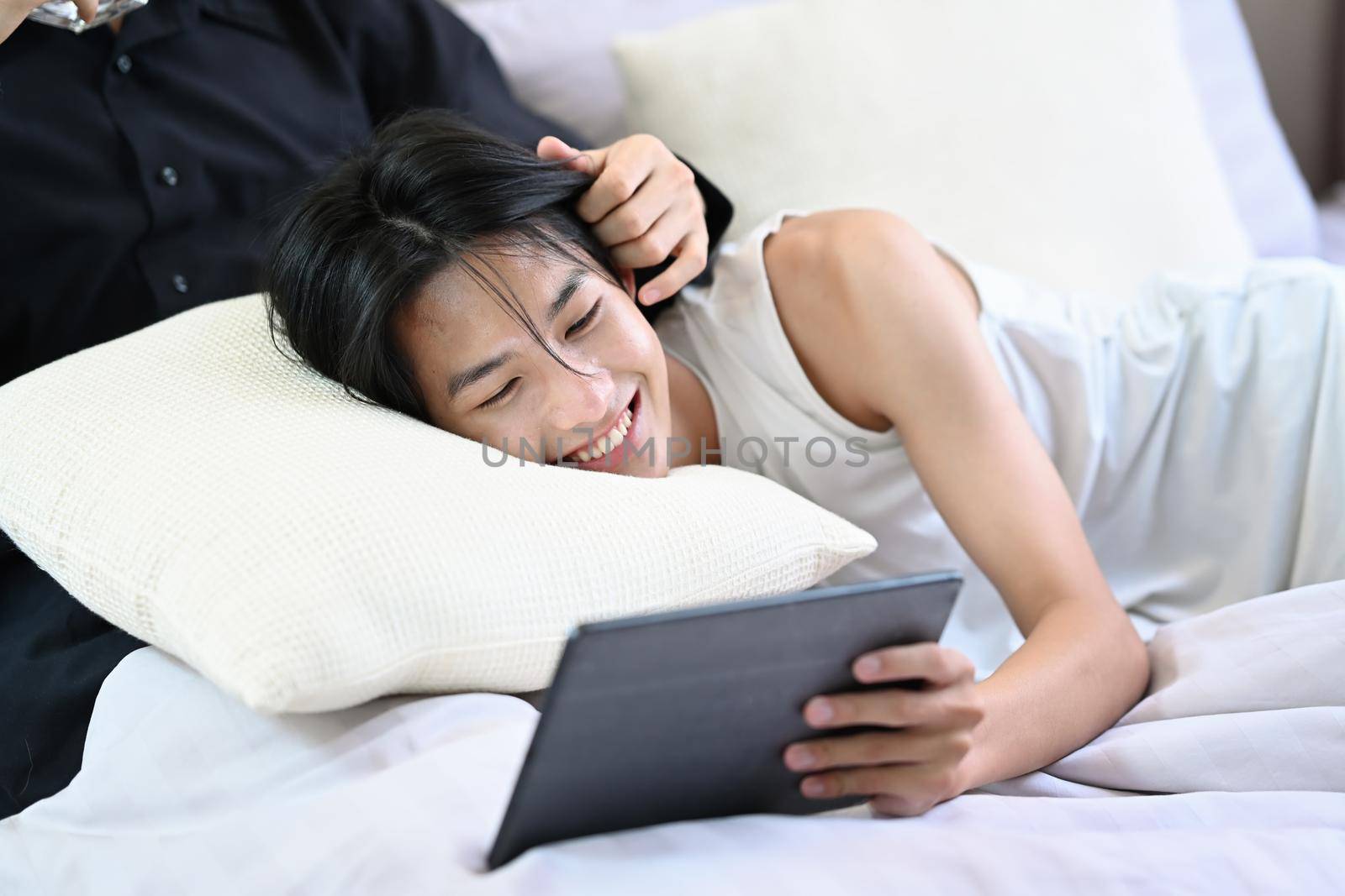 Happy homosexual couple using digital tablet on bed while spending leisure time together. LGBT, pride, relationships and equality concept.