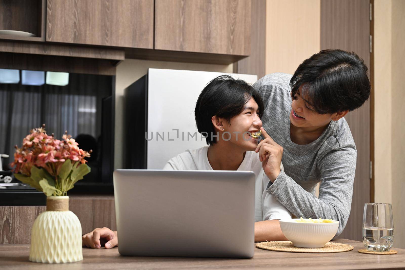 Homosexual couple having a happy morning conversation while using computer laptop in the kitchen.