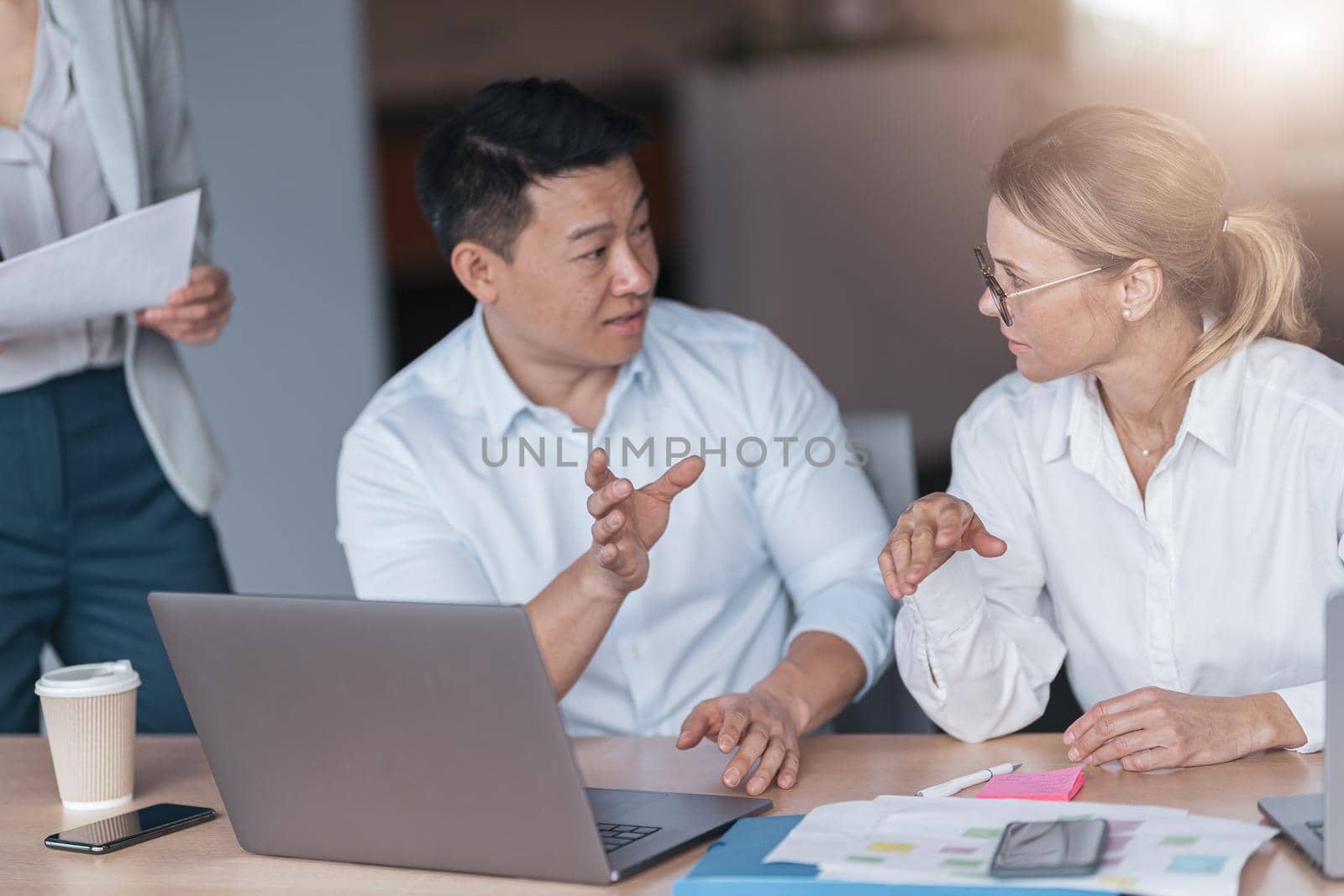 Confident asian office worker discussing work with mature business woman. Blurred background