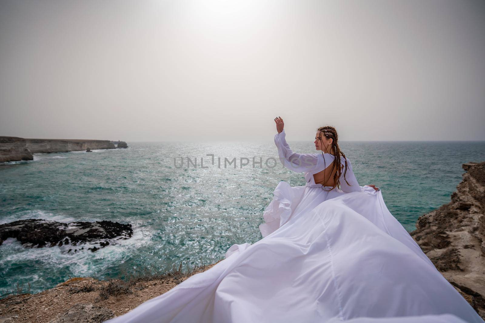 Happy freedom woman on the beach enjoying and posing in white dress. Rear view of a girl in a fluttering white dress in the wind. Holidays, holidays at sea