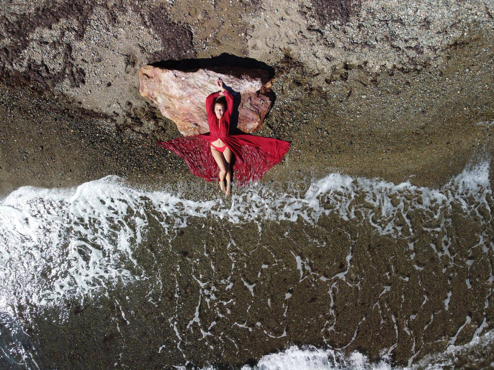 Young sensual blonde woman sitting on the rock near water at sea and enjoys the sea waves on background of two volcanic rocks, like in Iceland. Dreams holidays and weekend vacation in summer time