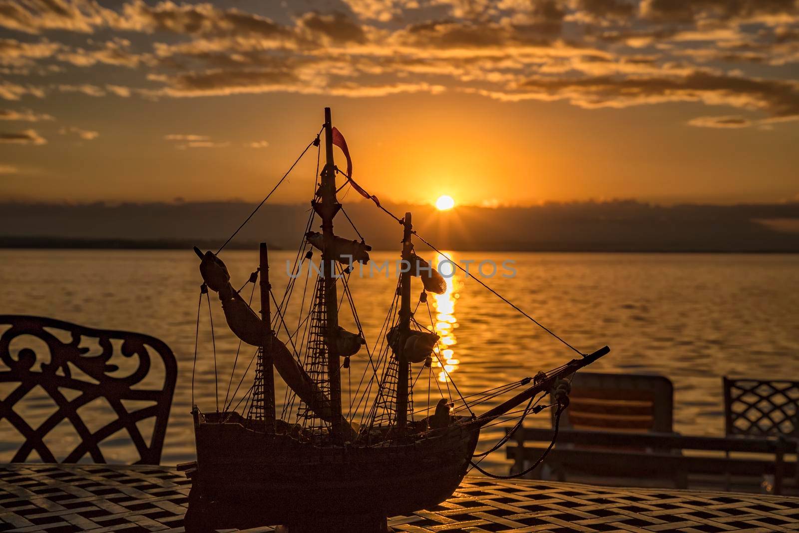 A silhouette of a chair and ship toy on a table at sunrise at the sea beach