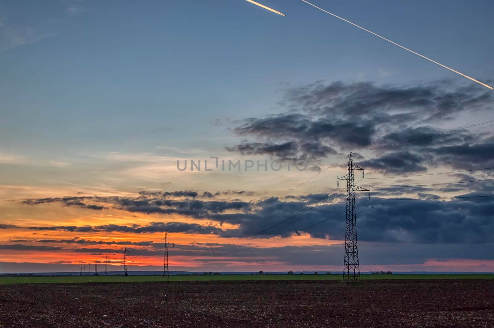 Poles and overhead power lines silhouettes in the dusk. Electricity generation and distribution. Electric power industry and nature concept