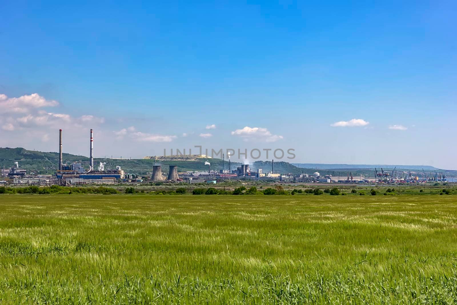 day view of a factory in the middle of a green rice field. Factory pipes polluting air on a silent.
