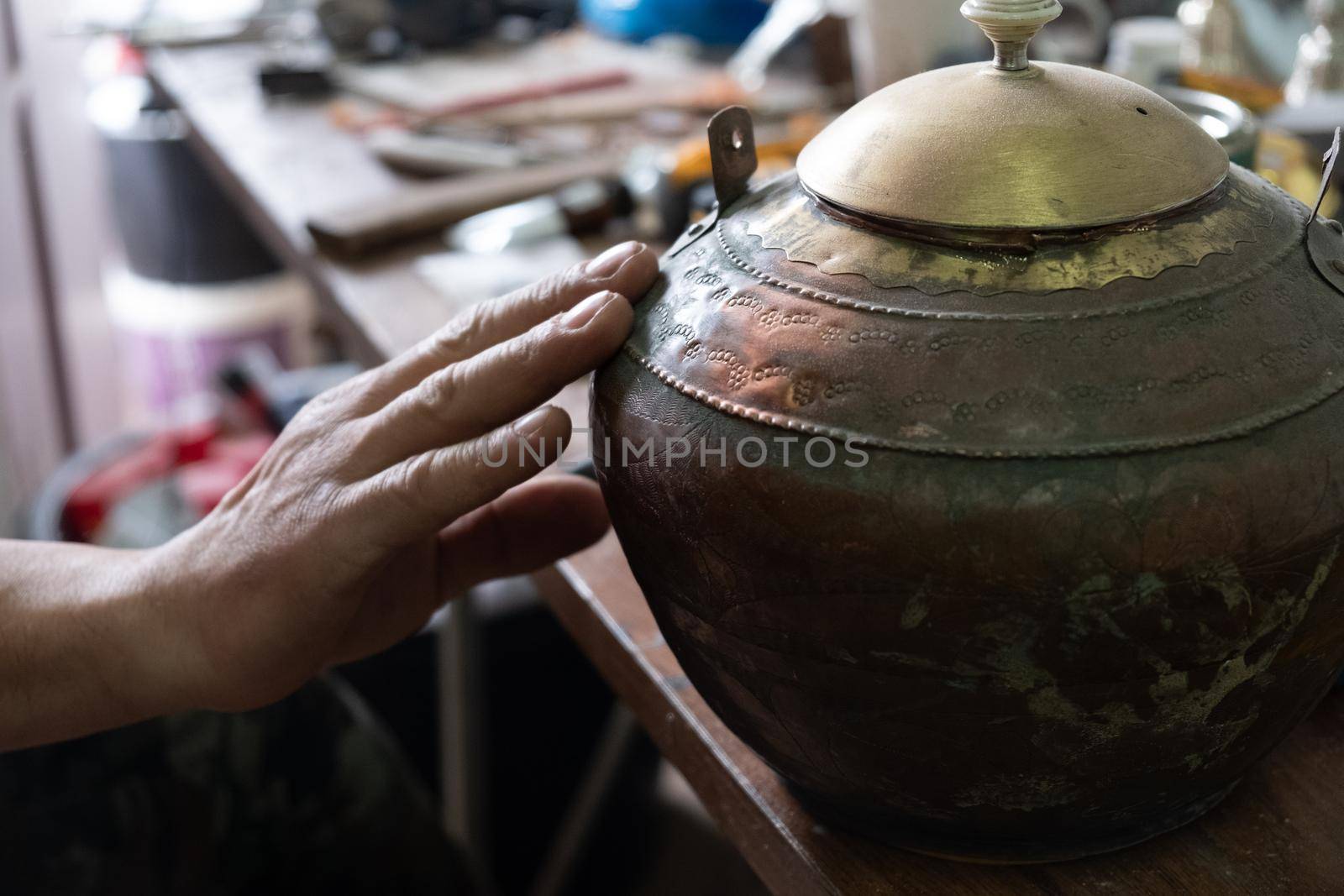 Restoration of an old jug of metal and other antiques, a man's hand touches the jug, in a workshop