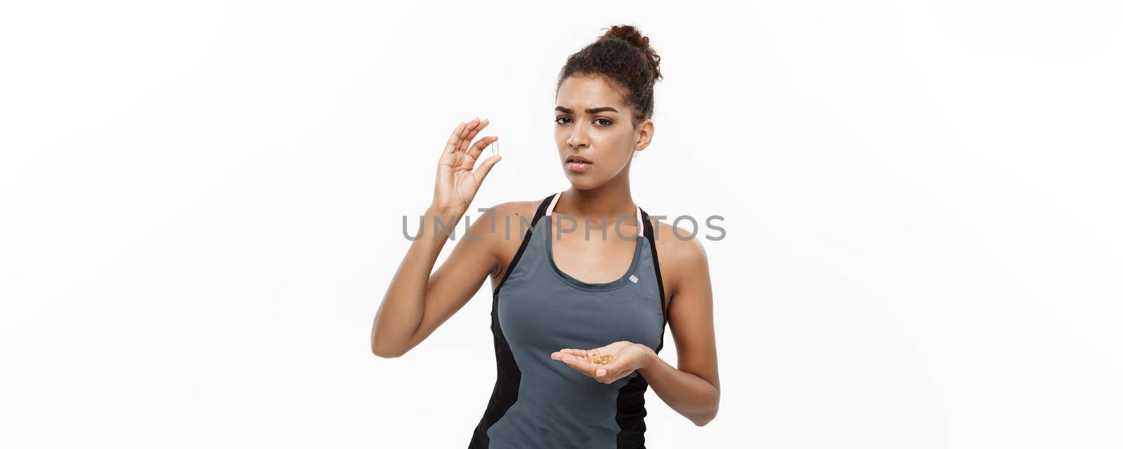 Healthy and Fitness concept - Closeup portrait of beautiful African American taking a pill of Cod liver oil. Isolated on white studio background. by Benzoix