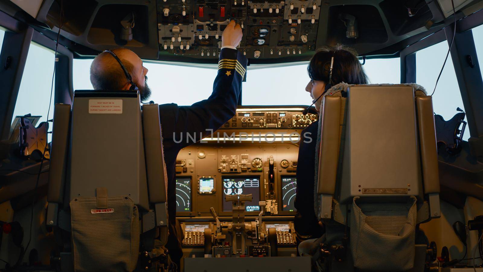 Male captain fixing altitude and longitude levels to fly airplane, using control panel command to takeoff. Aviators flying aircraft with dashboard navigation and windscreen buttons.
