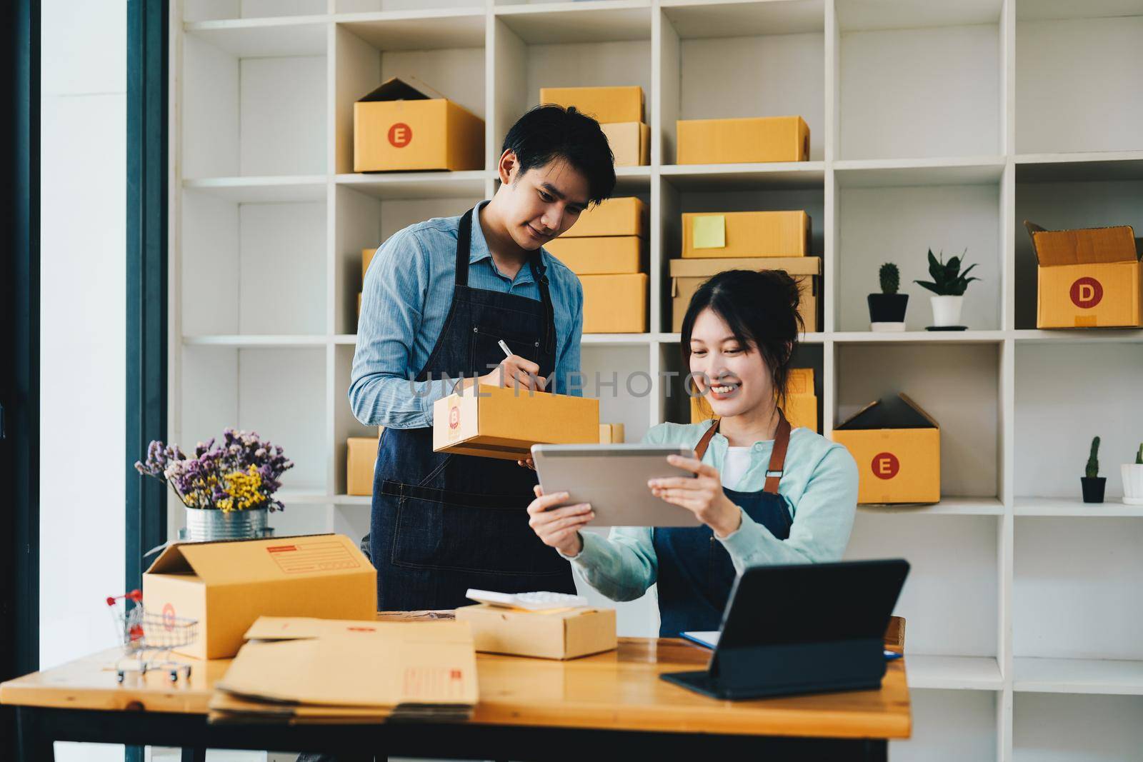 Asian couple doing online business together at home. Helping to pack products into cardboard boxes. family concept, modern business, small entrepreneurs, online delivery.