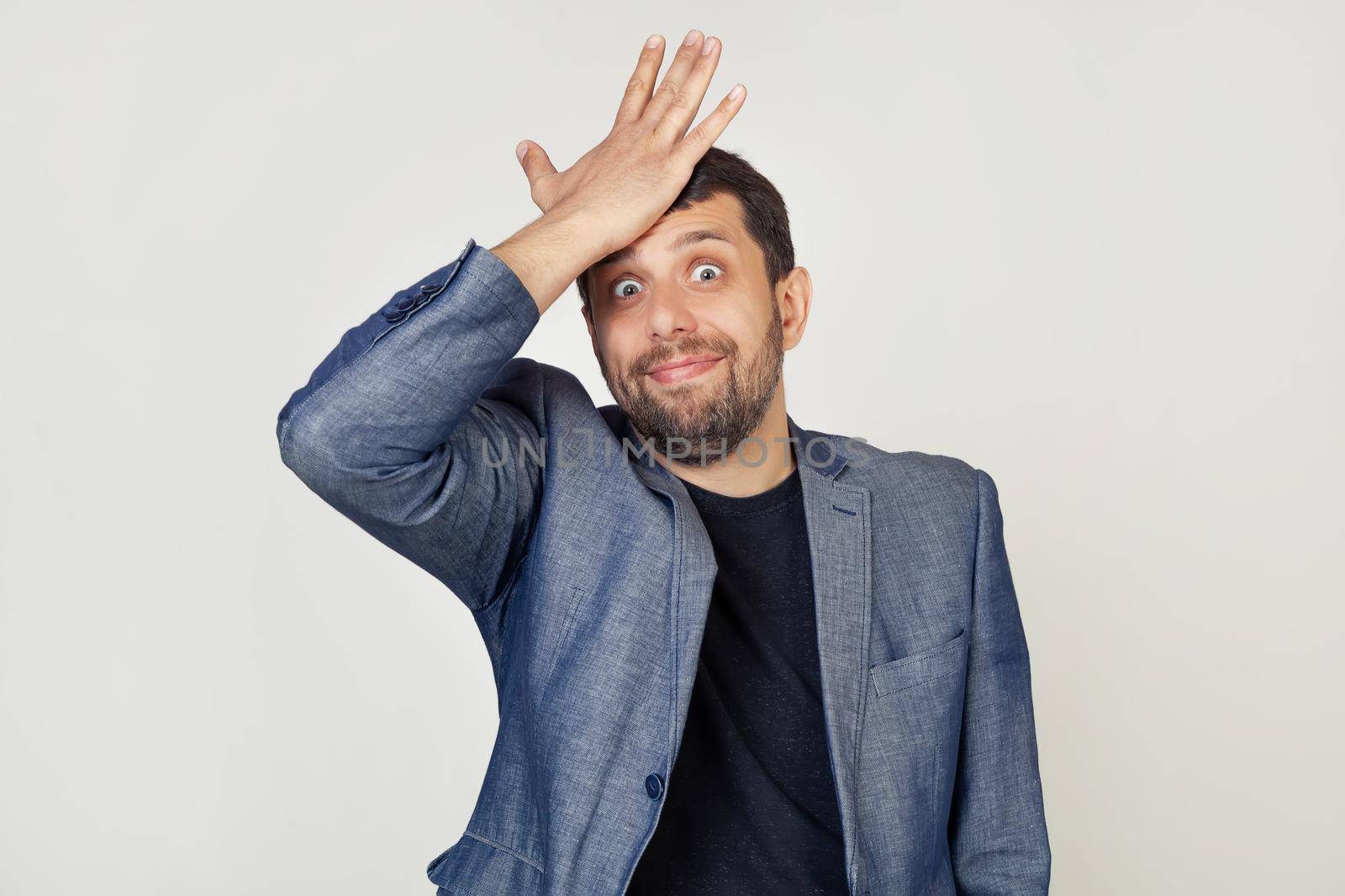Young businessman man with a beard in a jacket, with an expression of frustration and misunderstanding. Surprised putting his hand on his head for a mistake. Forgot, bad memory concept.