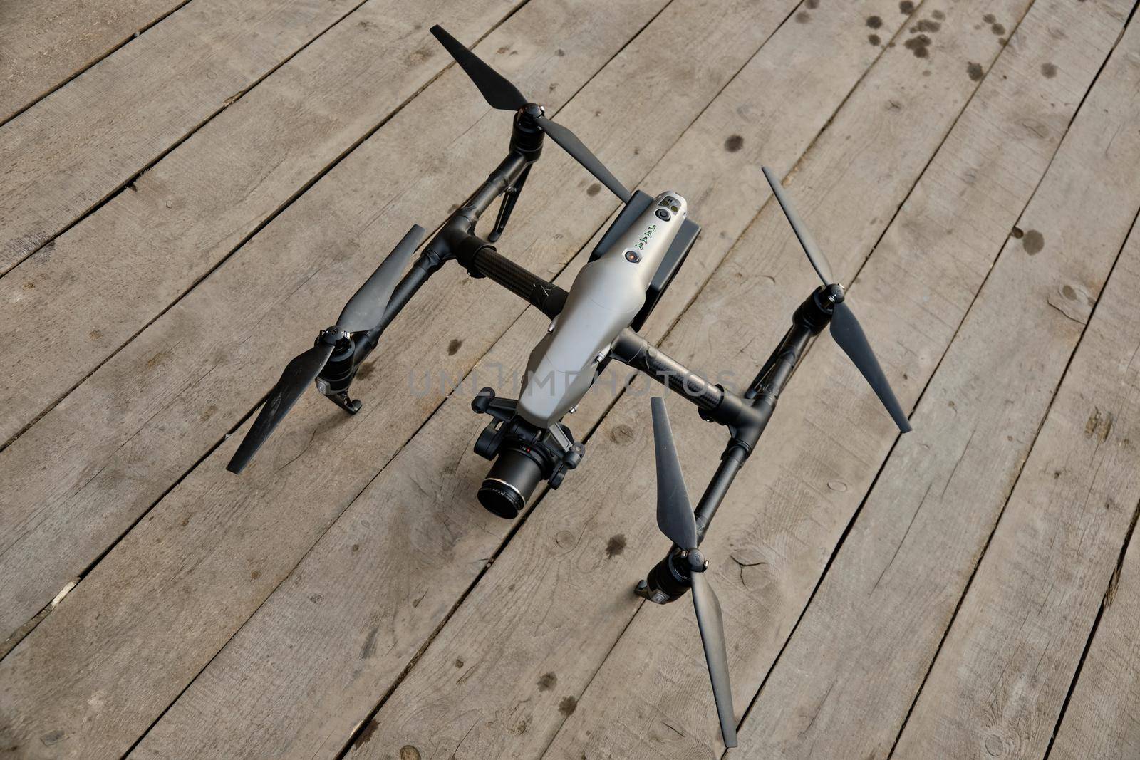 A professional drone stands on a wooden floor, preparing for flight, above view