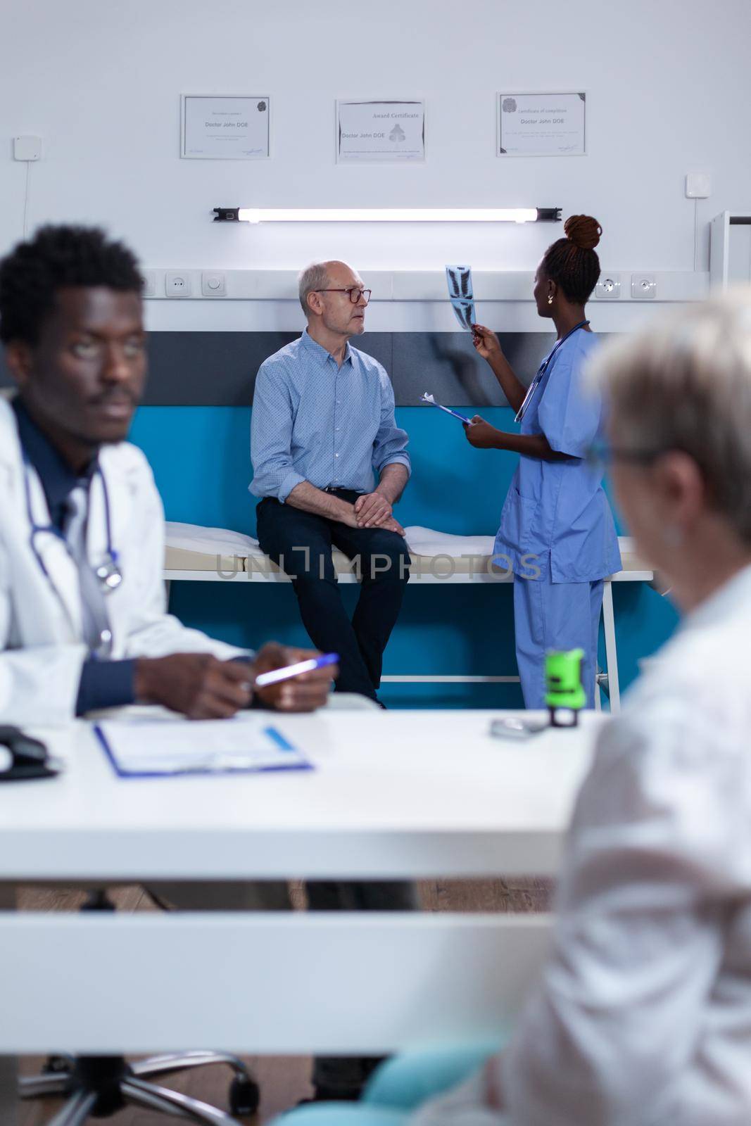 Healthcare facility nurse examining x-ray scan image of elderly patient with acute leg pain. Retired man listening to nurse talking about consultation appointment and treatment schedule