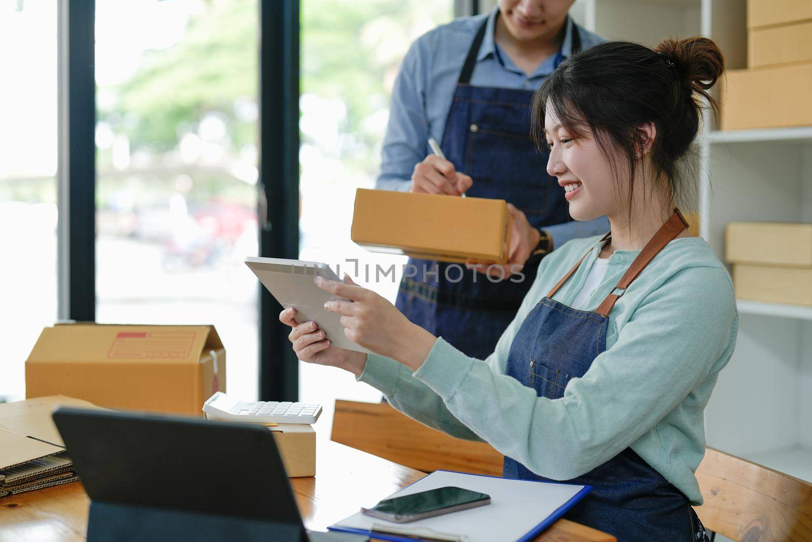 Asian couple doing online business together at home. Helping to pack products into cardboard boxes. family concept, modern business, small entrepreneurs, online delivery.