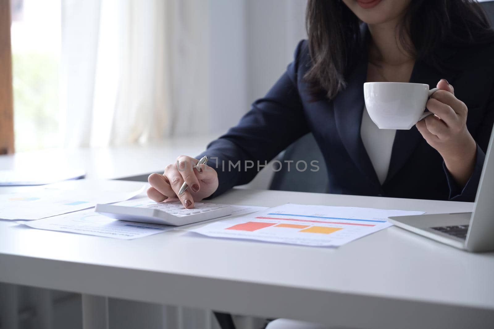 Cropped shot businesswoman drinking coffee and preparing annual financial report at office desk.