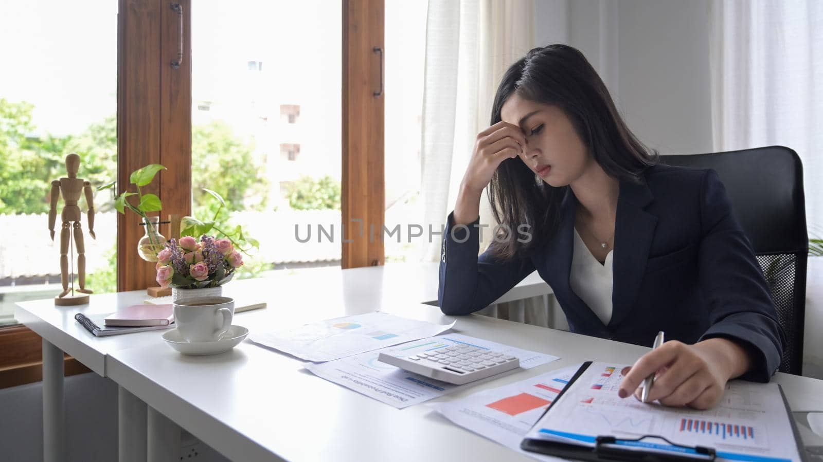 Young businesswoman looking worried, tired and overwhelmed while working at office desk.