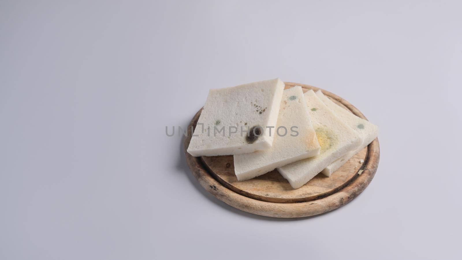 Moldy bread on wooden chopping board with white background.