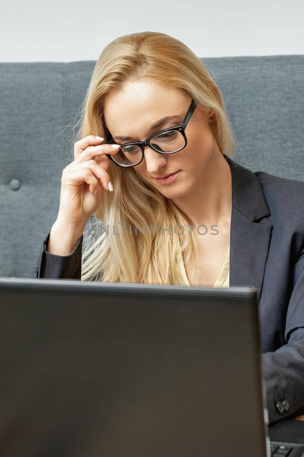 Busy business woman wearing eyeglasses working on laptop at home office.