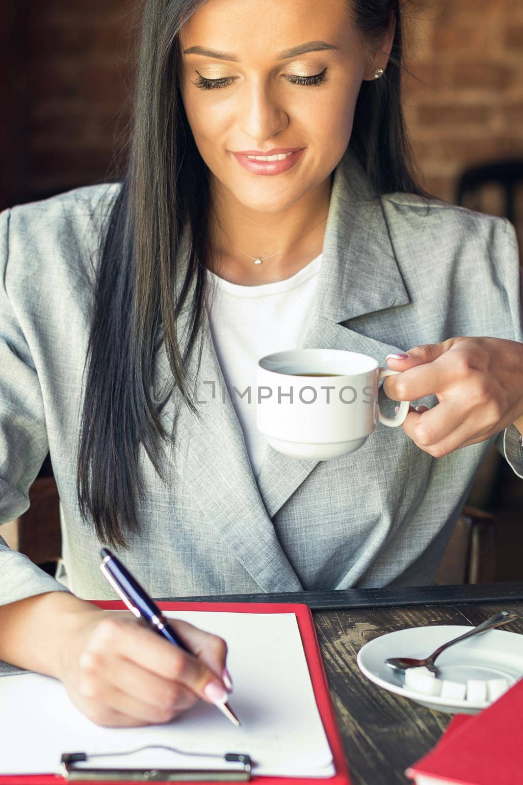 young businesswoman is writing plans on the notebook while holding cup of coffee at cafe, business concept