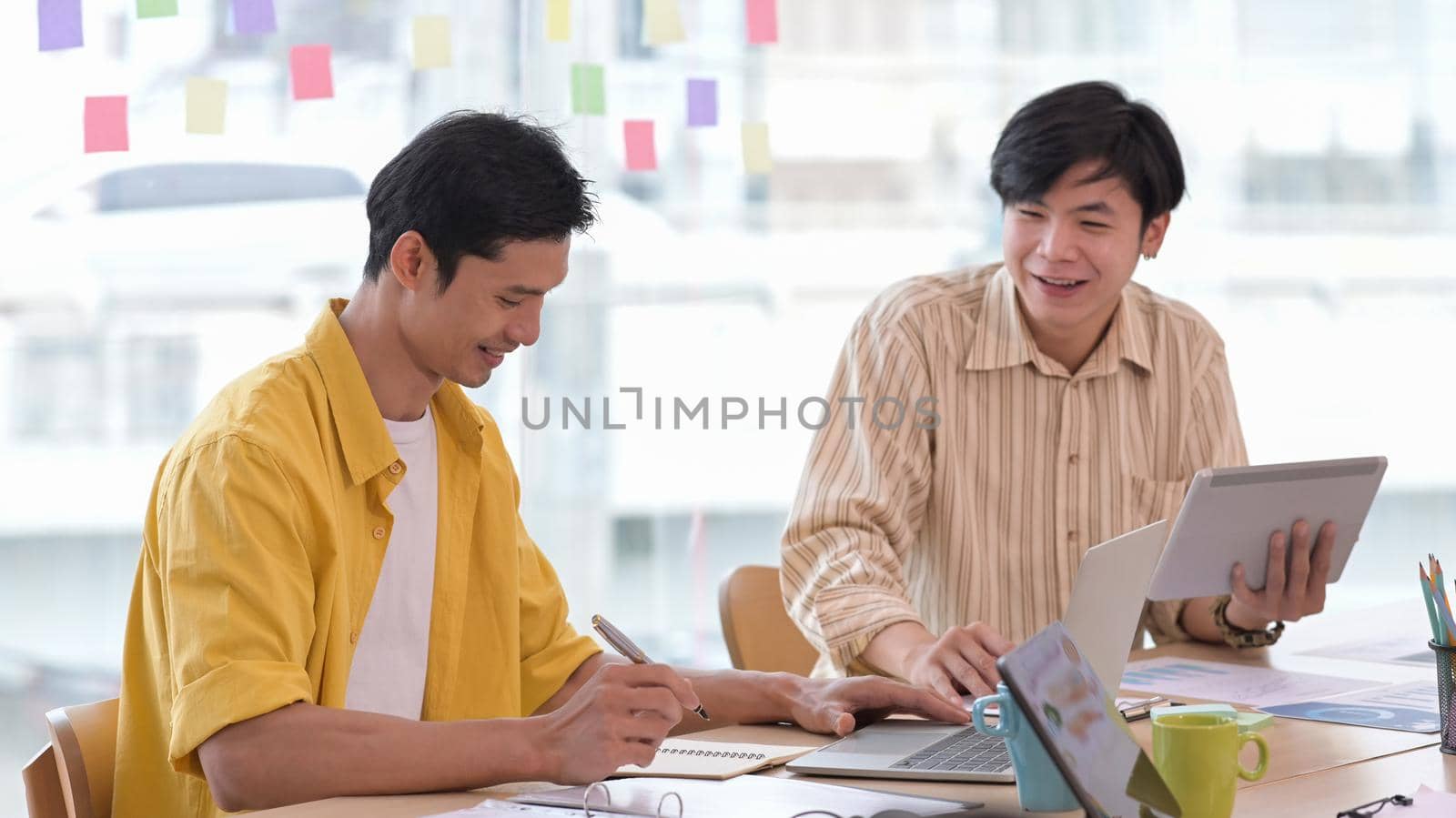 Two happy young creative man working together at modern workplace. by prathanchorruangsak