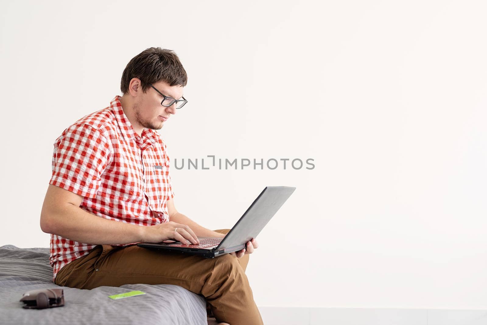 Online shopping concept. Young man sitting on the bed and shopping online using tablet, copy space