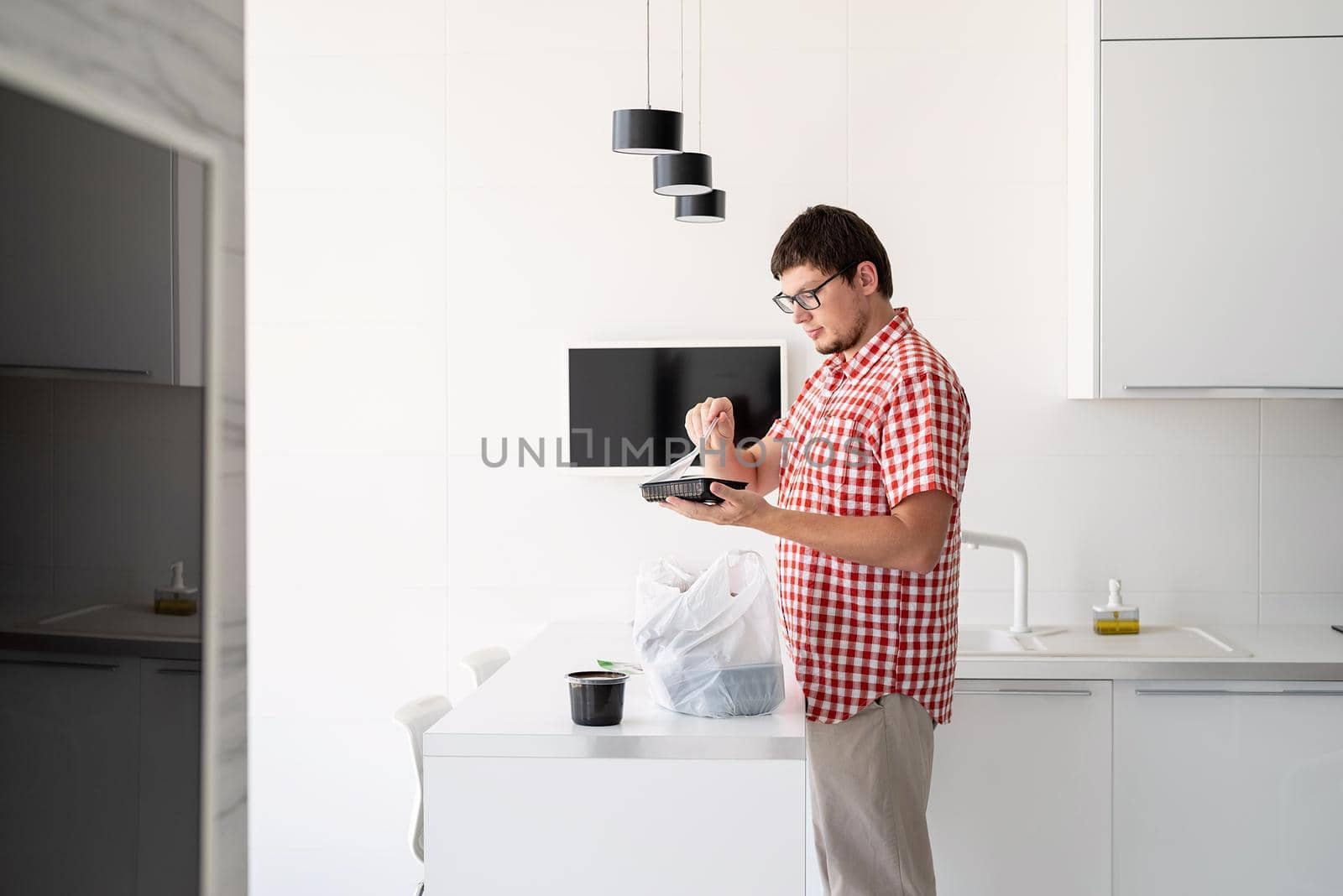 Delivery food, products to home. Shopping and healthy food concept. Young man in red plaid shirt holding a disposable plastic bag with food delivery at the modern kitchen