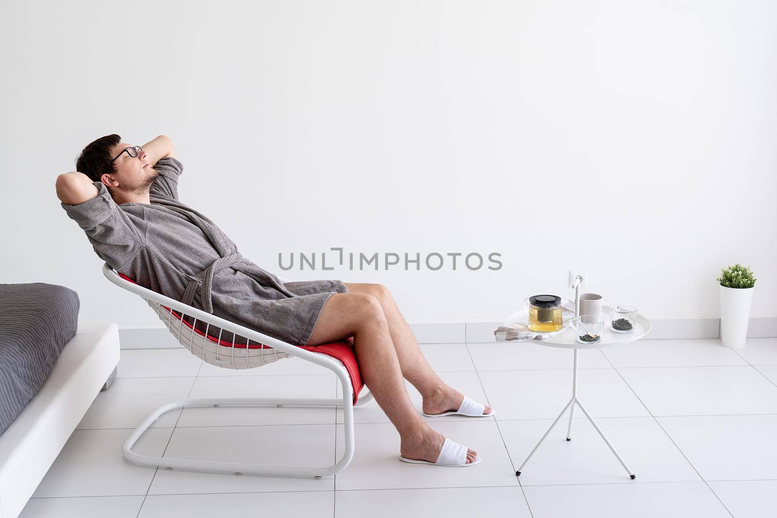 man siting in bathrobe making tea at home by Desperada