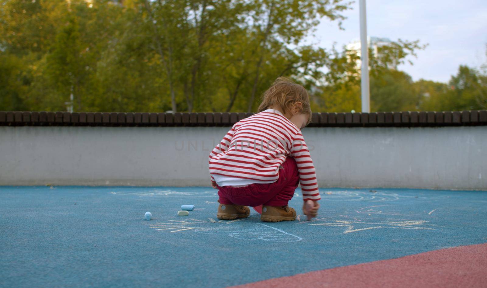 Small girl chalking on the playground in the park. Children's development concept