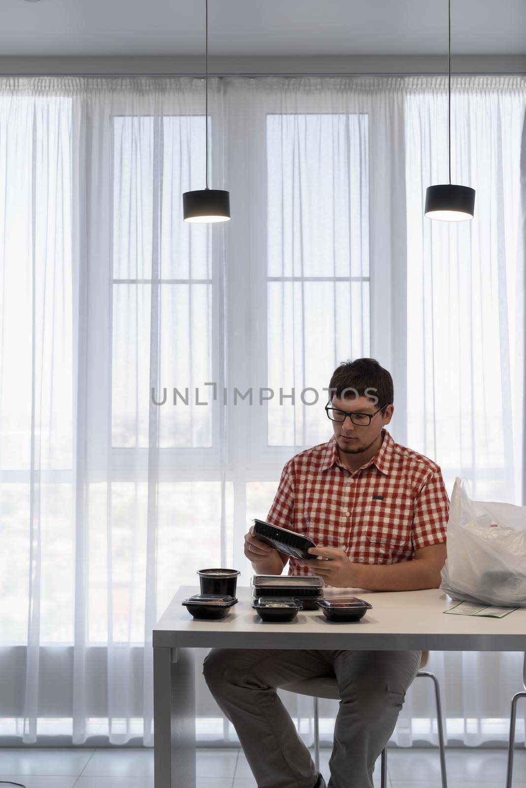 Delivery food, products to home. Shopping and healthy food concept. Young man in red plaid shirt Young man sorting food delivery boxes at the modern kitchen at the modern kitchen