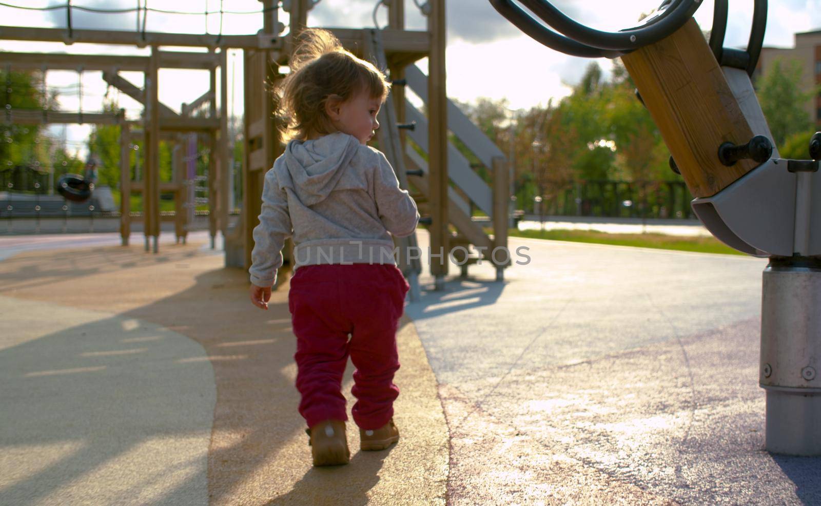 Baby girl near carousel in the park. Back light.