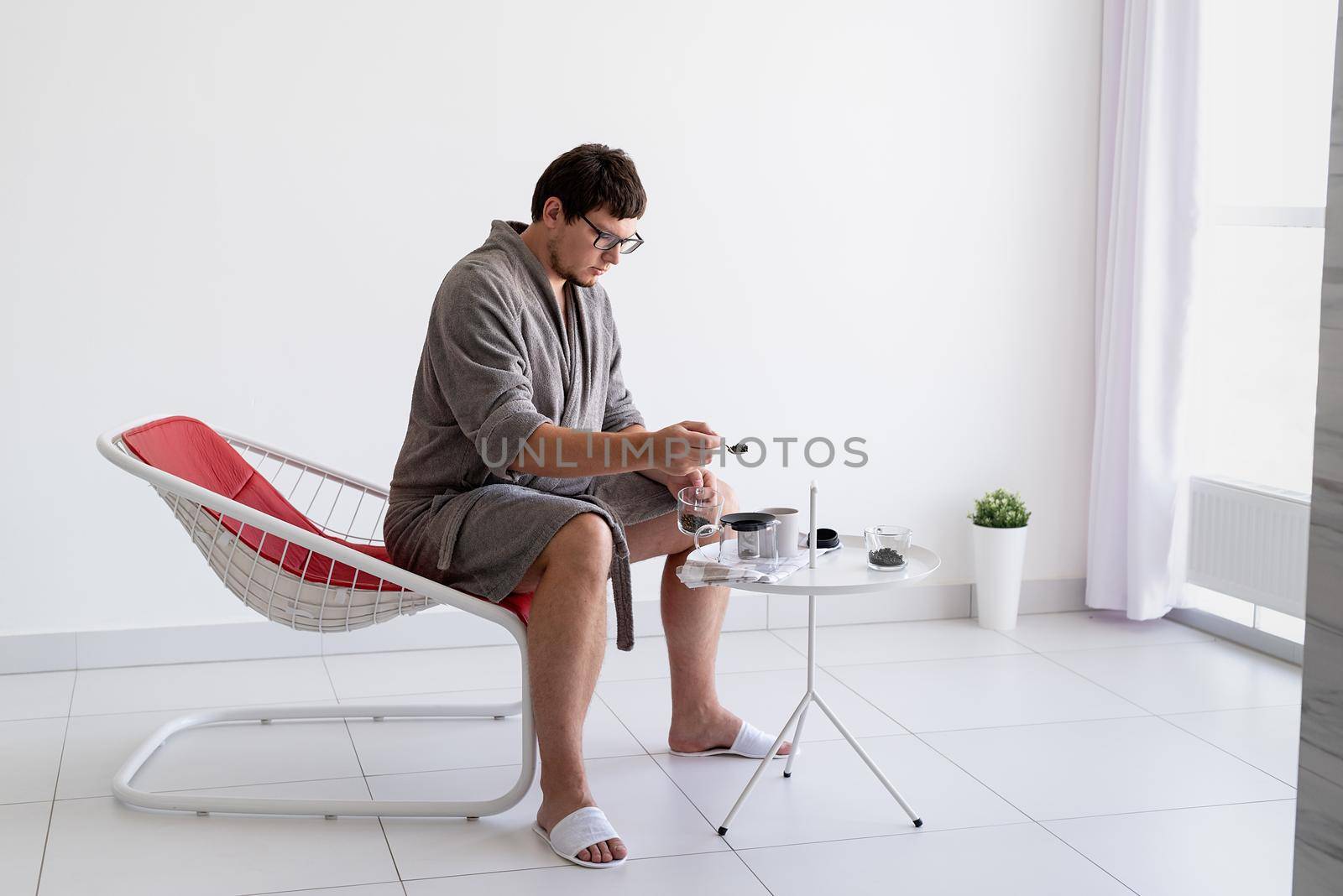 Young caucasian man in gray bathrobes sitting in the living room relaxing and brewing green tea