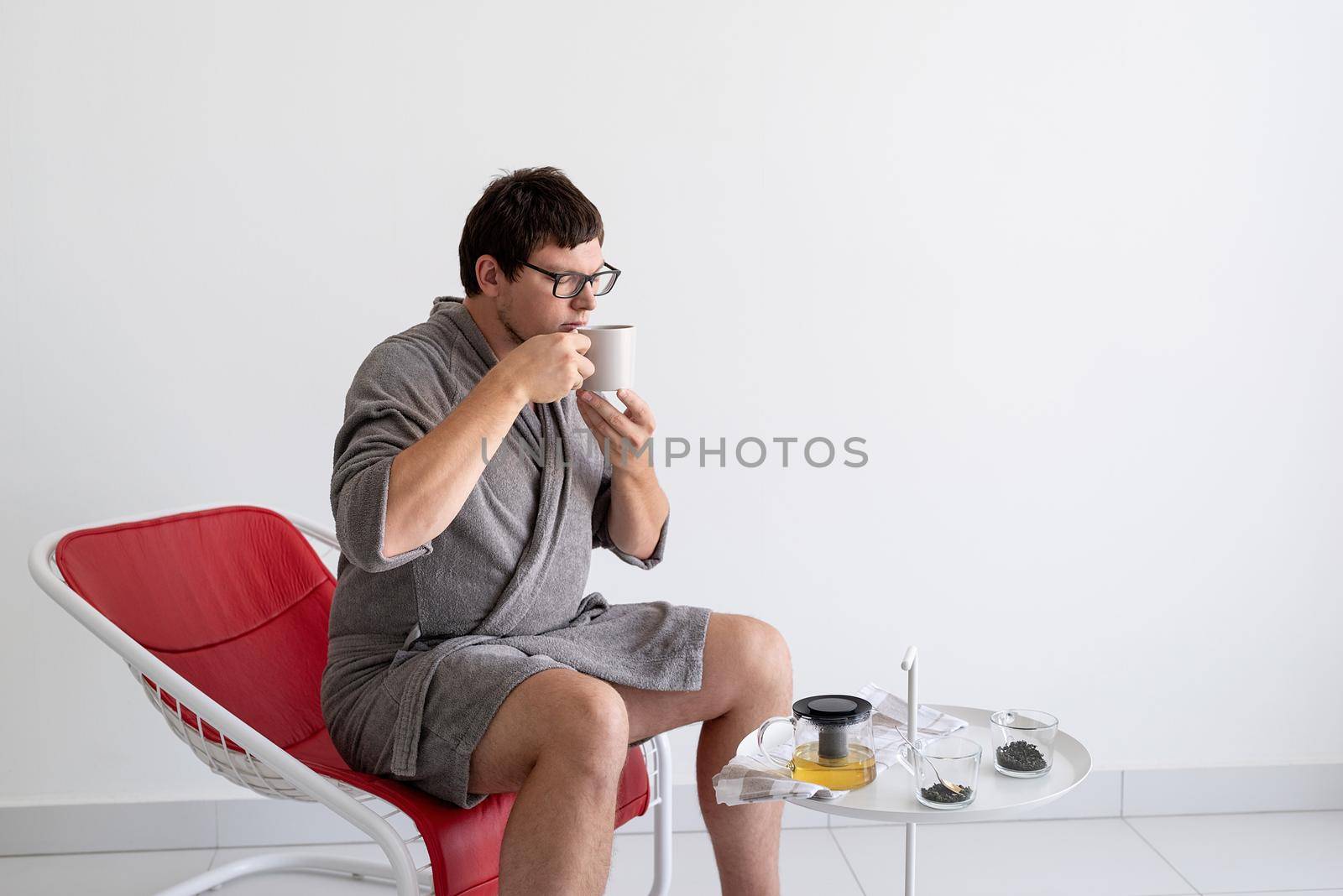 Young caucasian man in gray bathrobes sitting in the living room relaxing and brewing green tea
