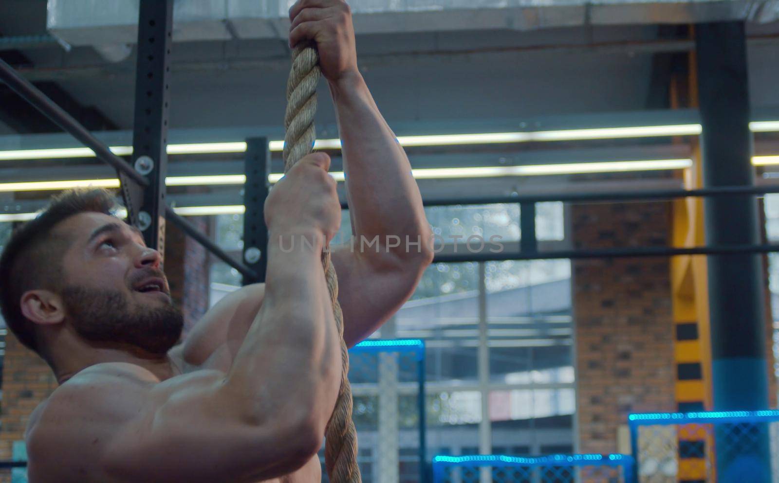 The male athlete is climbing a rope. Bodybuilder in the gym.