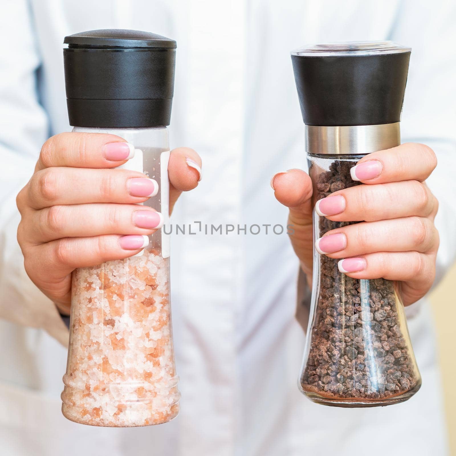 Female hands holding salt and pepper mills wearing white shirt on yellow background.