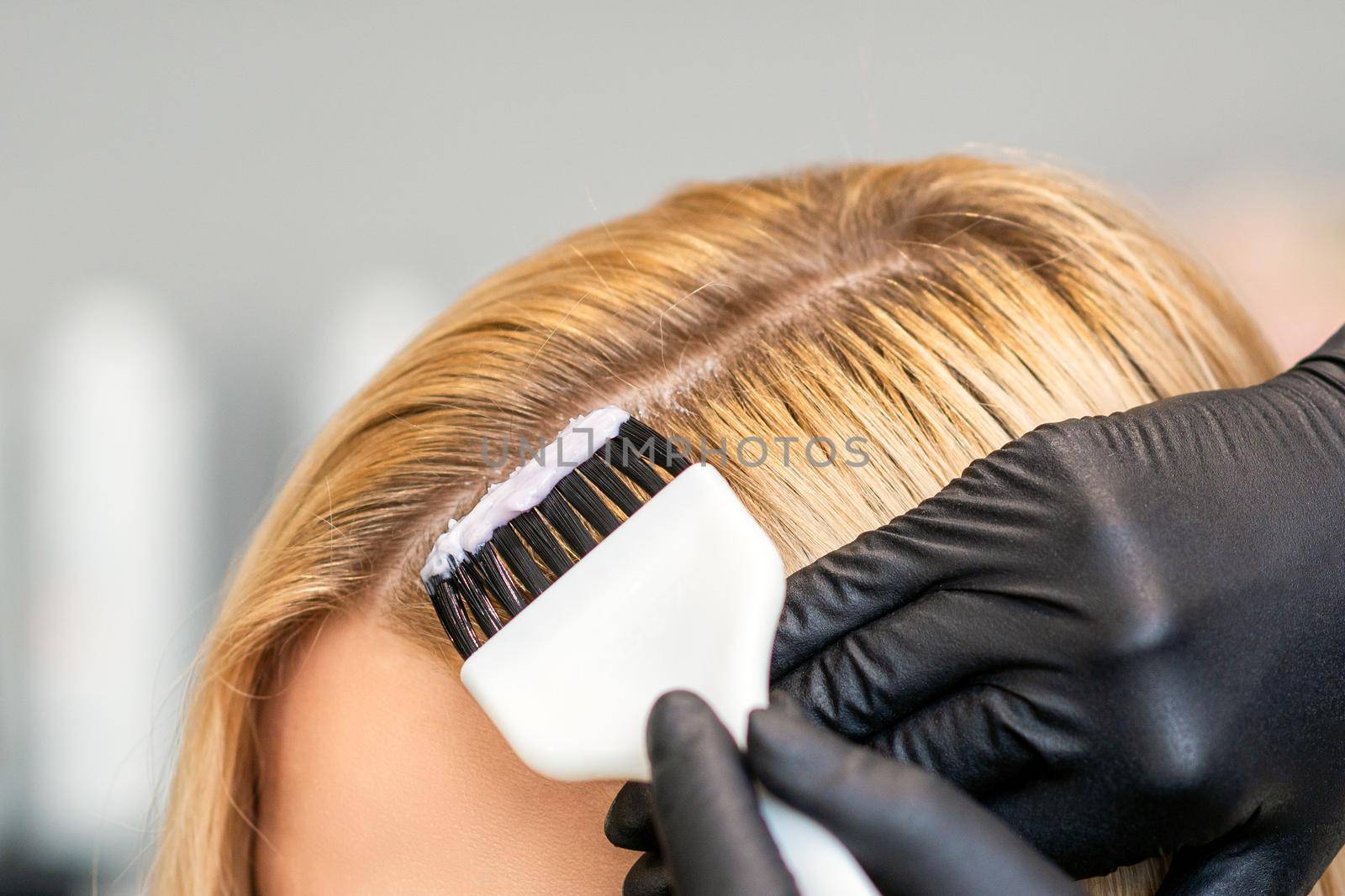 Hands of hairdresser dyeing hair of woman with brush at beauty salon.