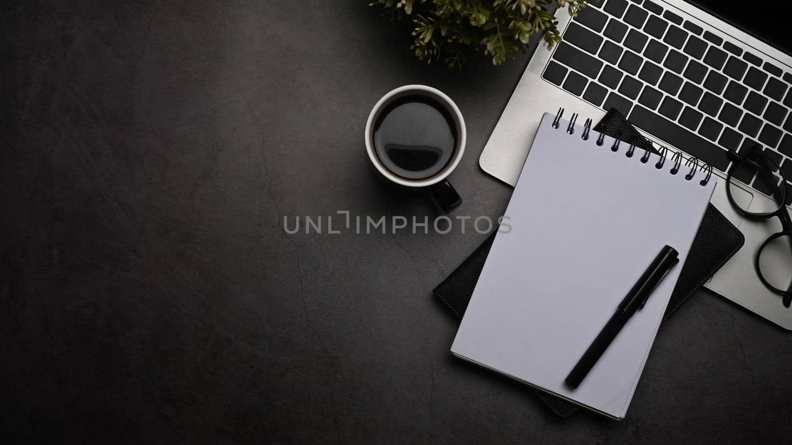 Notebook and pen on dark modern office desk with top view shot.