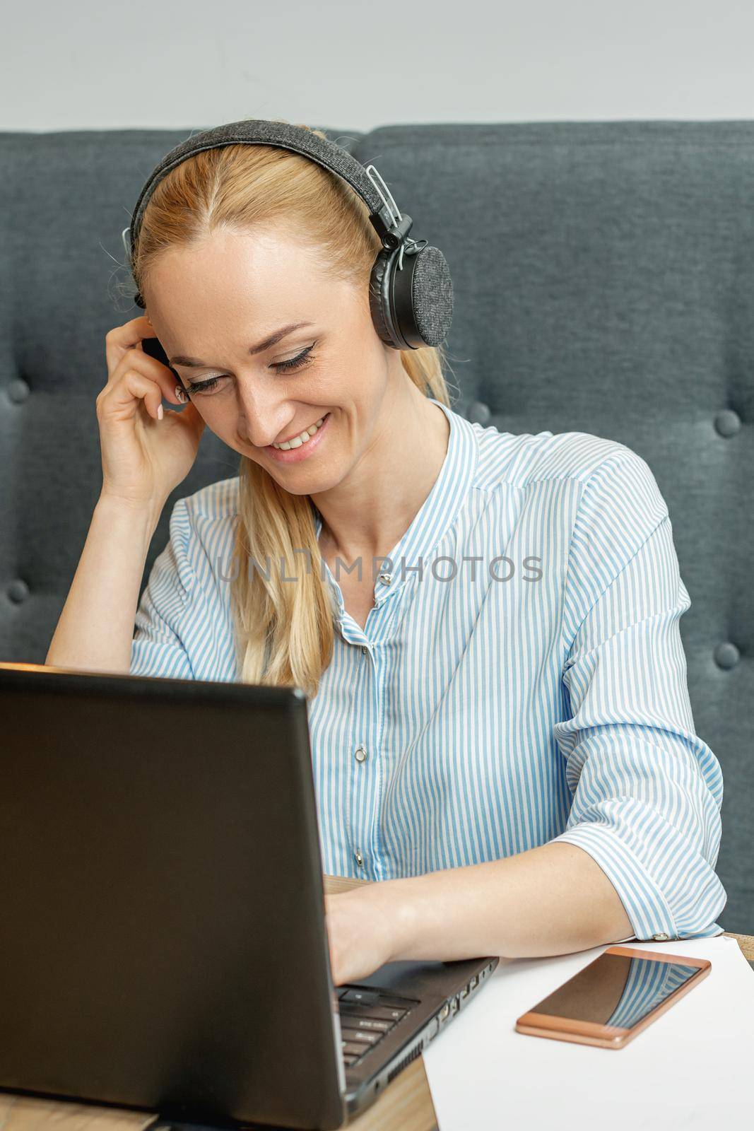 Happy young woman wearing headphones looking on laptop screen during online training and video conference at home office.