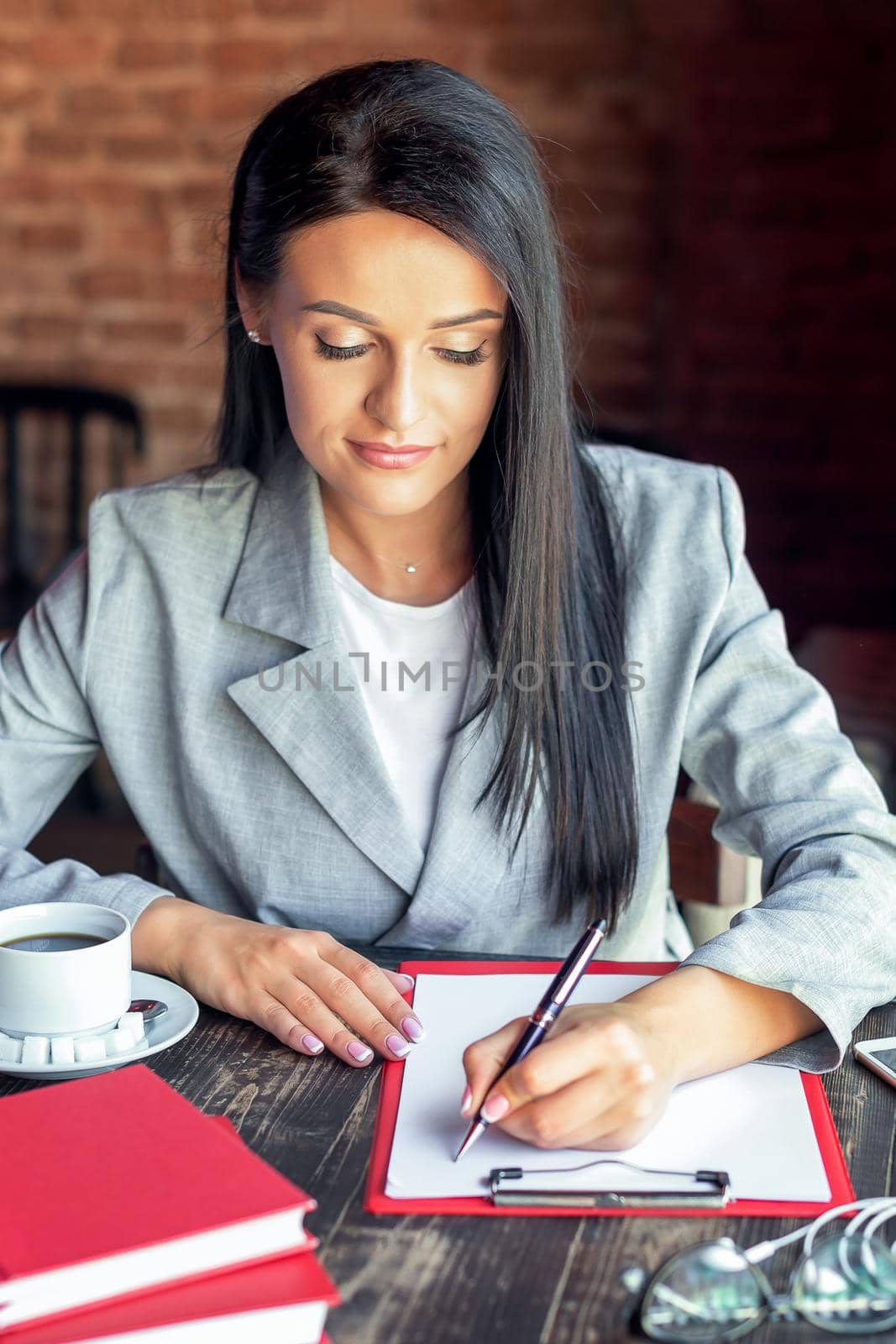 Beautiful young business woman is writing on white paper in the cafe.