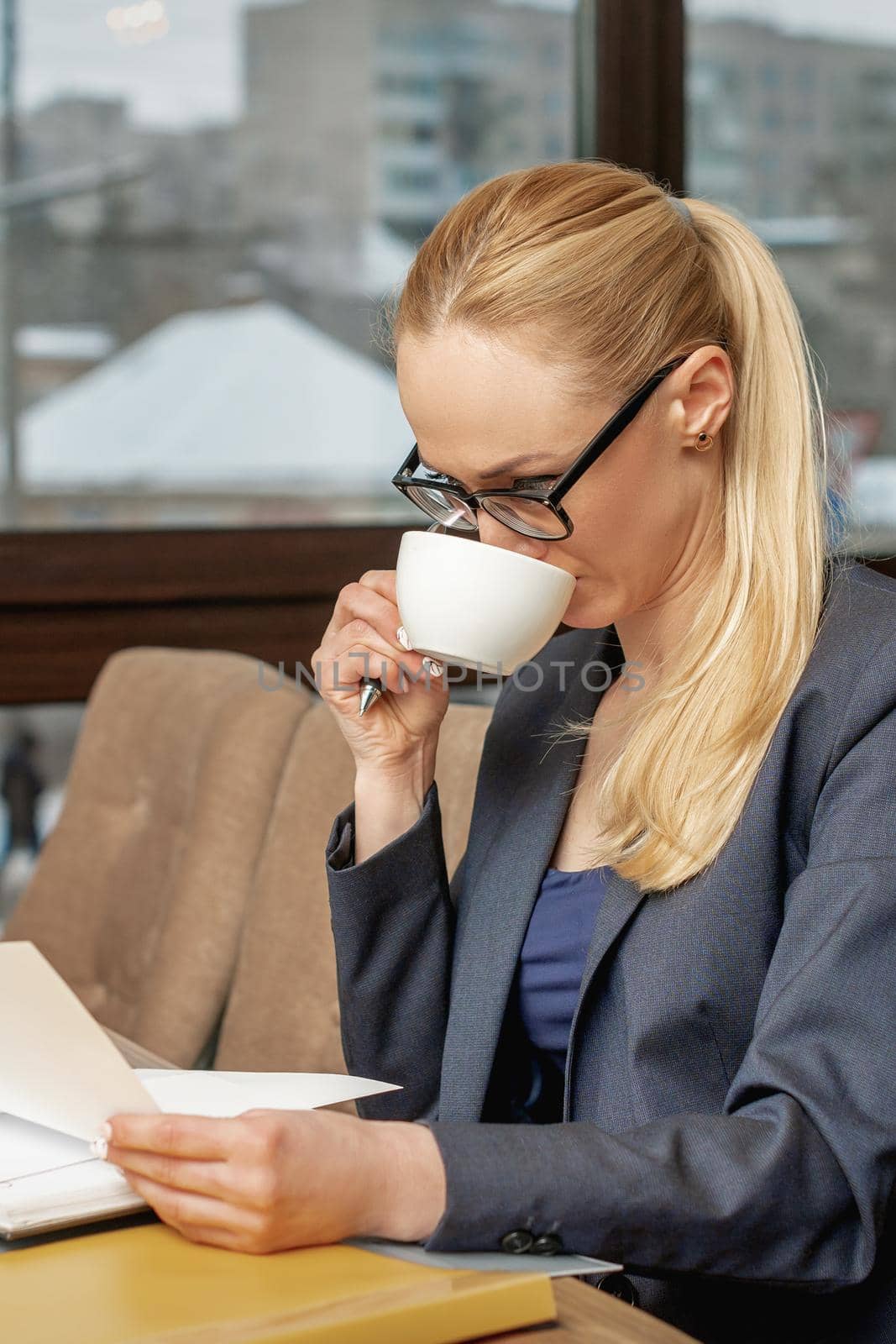 Business woman reading news working with documents and drinking coffee in office.