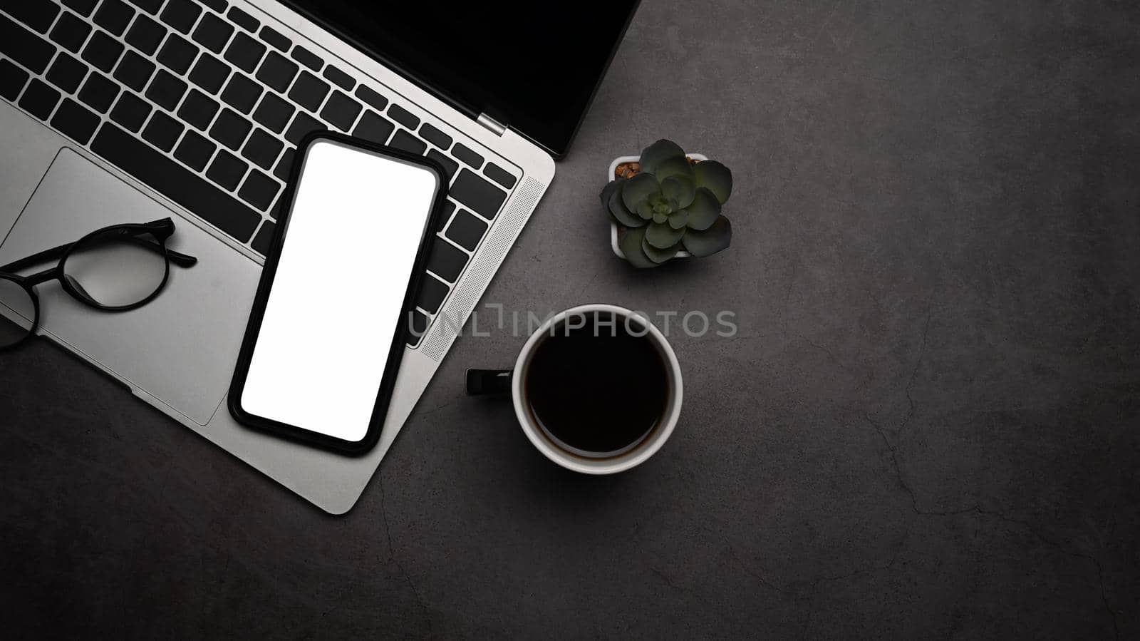 Stylish workplace with smart phone, laptop computer and coffee cup on dark stone background. Top view.