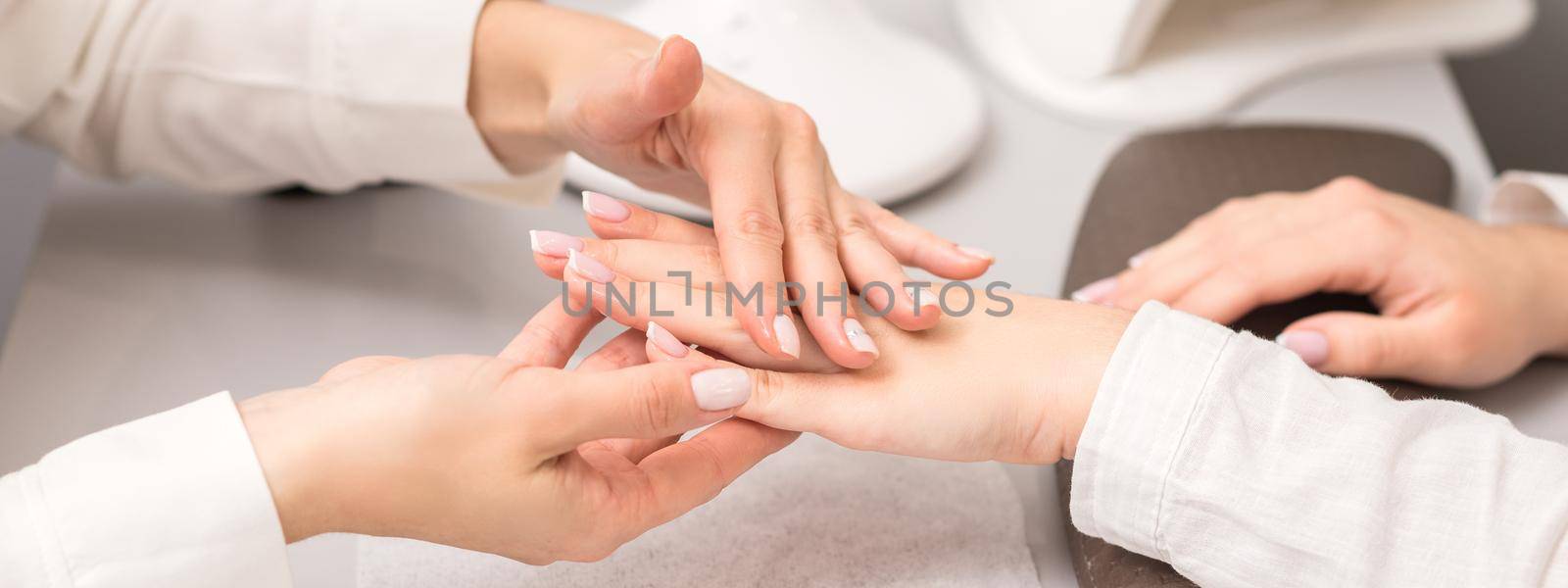 Hands and nails of young woman receiving oil massage by beautician at beauty salon.