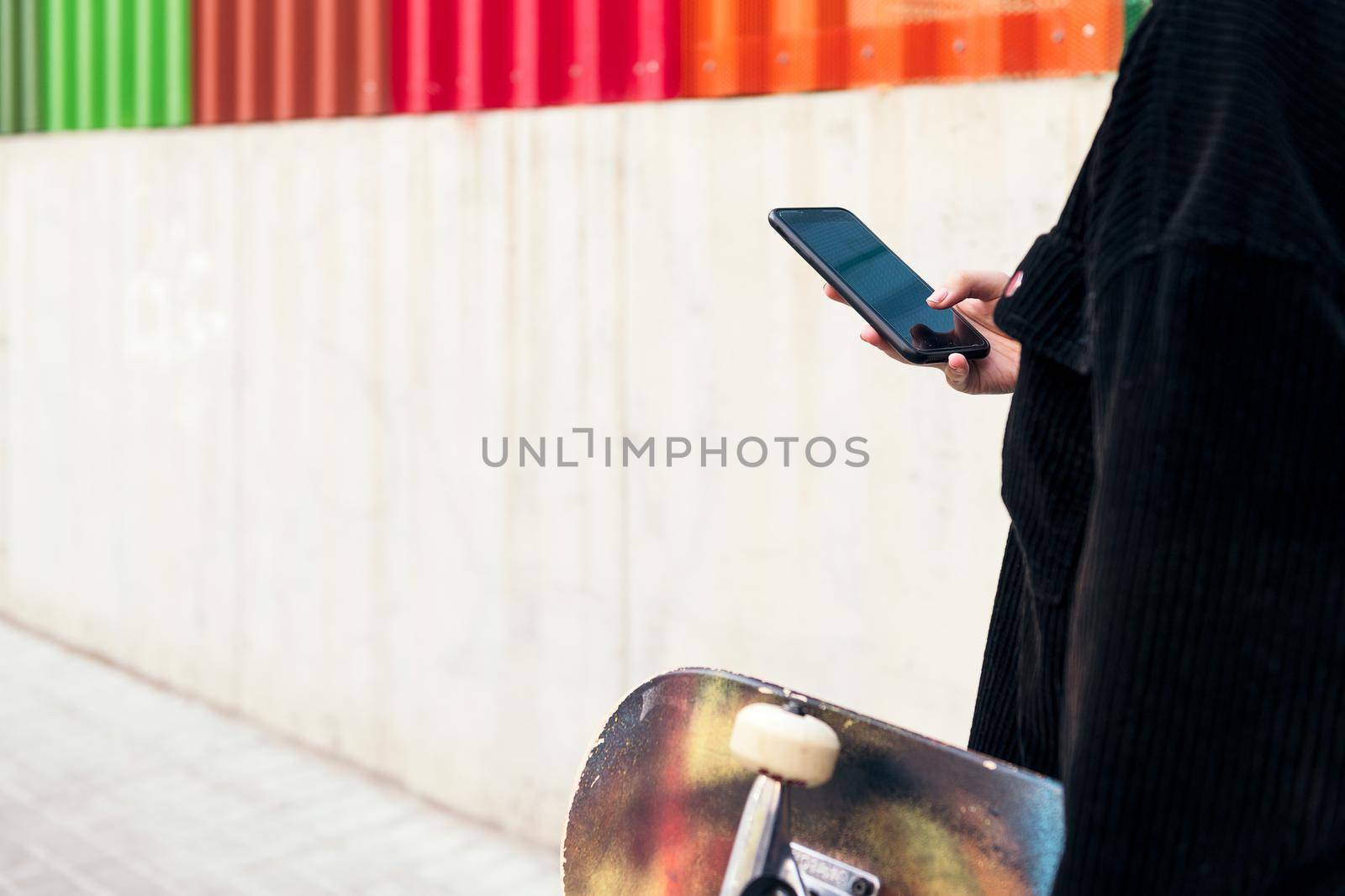 unrecognizable young woman typing on the mobile phone while walking down the street with her skateboard in her hand