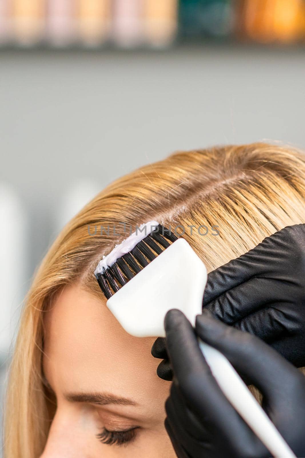 Hands of hairdresser dyeing hair of woman with brush at beauty salon.