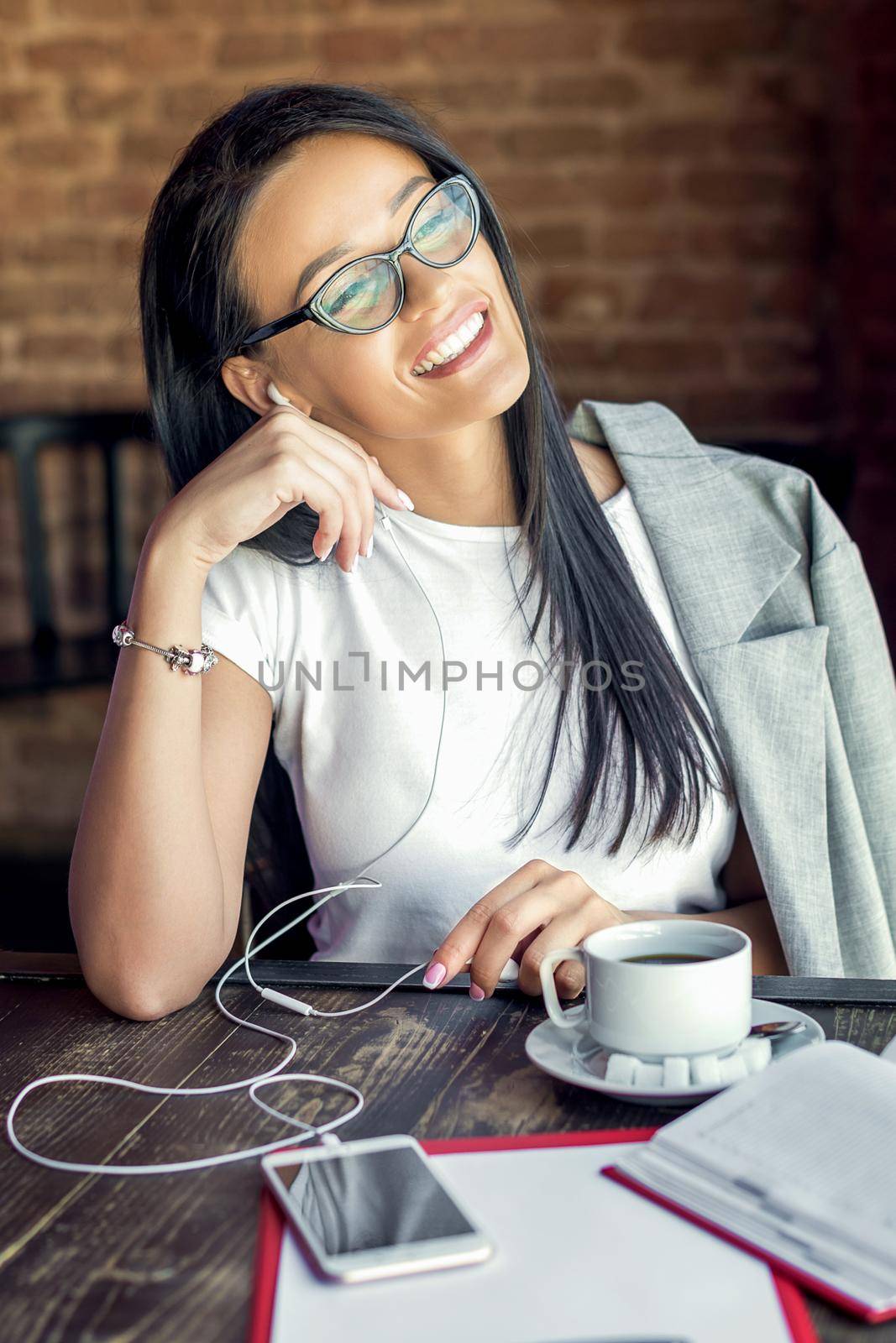 Beautiful smiling woman in glasses is listening music by her smartphone at cafe. Lifestyle concept