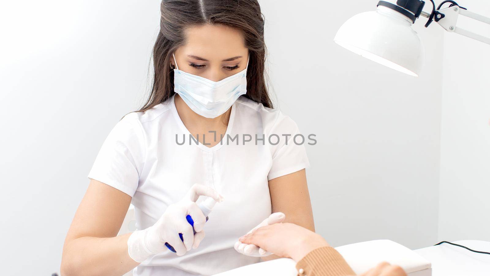 Manicurist is applying antiseptic on client's hands in manicure salon.