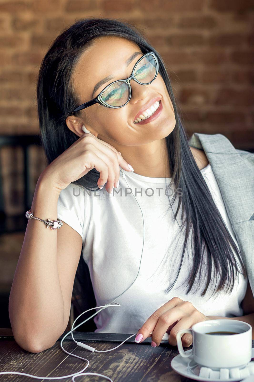 Beautiful smiling woman in glasses is listening music by her smartphone at cafe. by okskukuruza