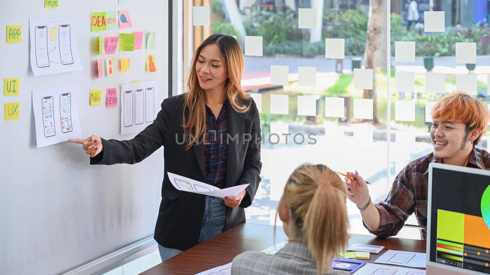 Confident female web developer is presenting sketch, prototype, framework, layout future app design project on whiteboard. by prathanchorruangsak