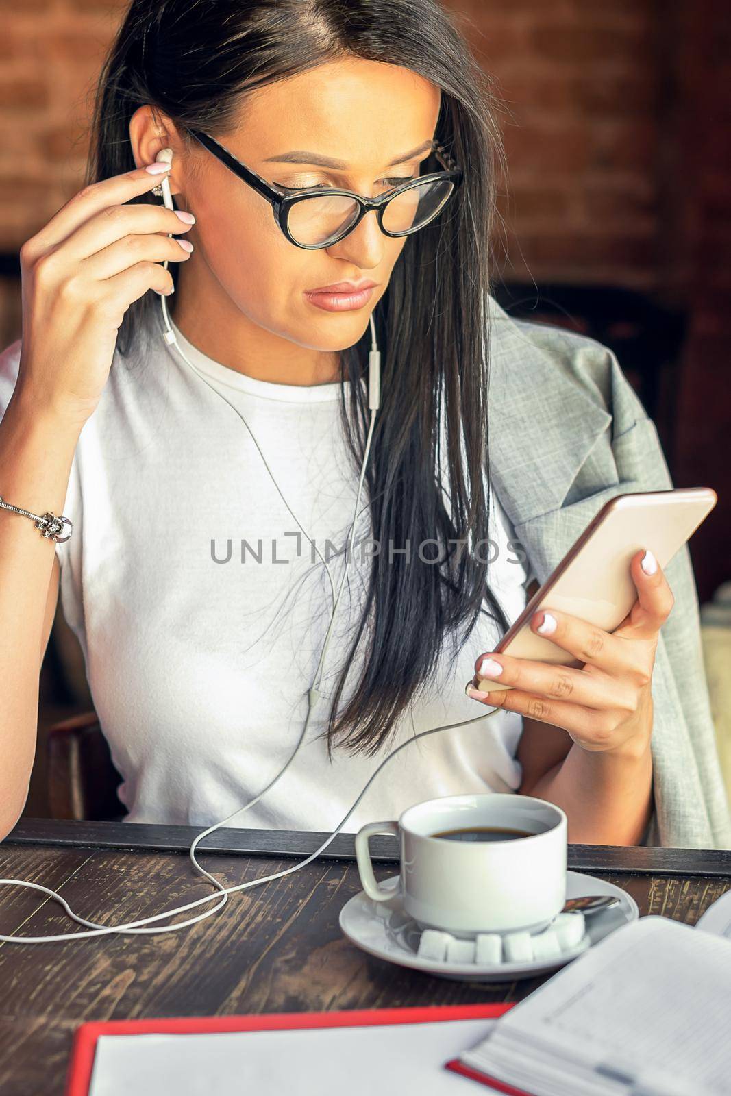 Beautiful woman in glasses is listening music by her smartphone at cafe. by okskukuruza