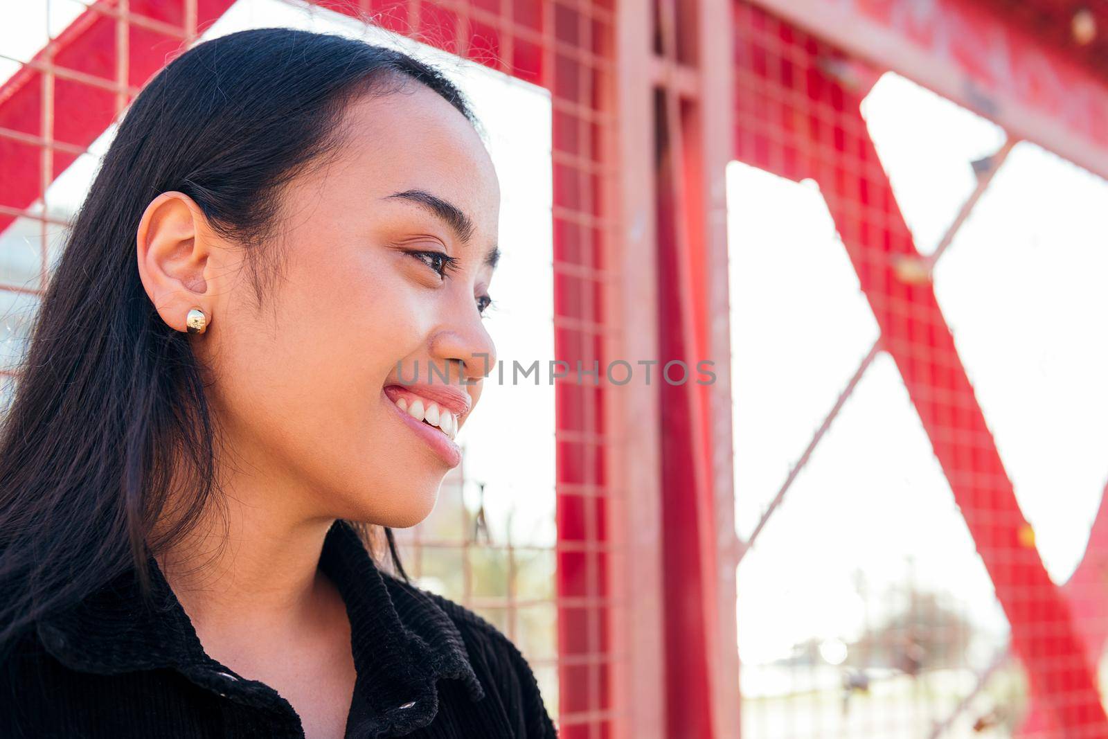portrait of a smiling young asian woman outdoors leaning against a red fence