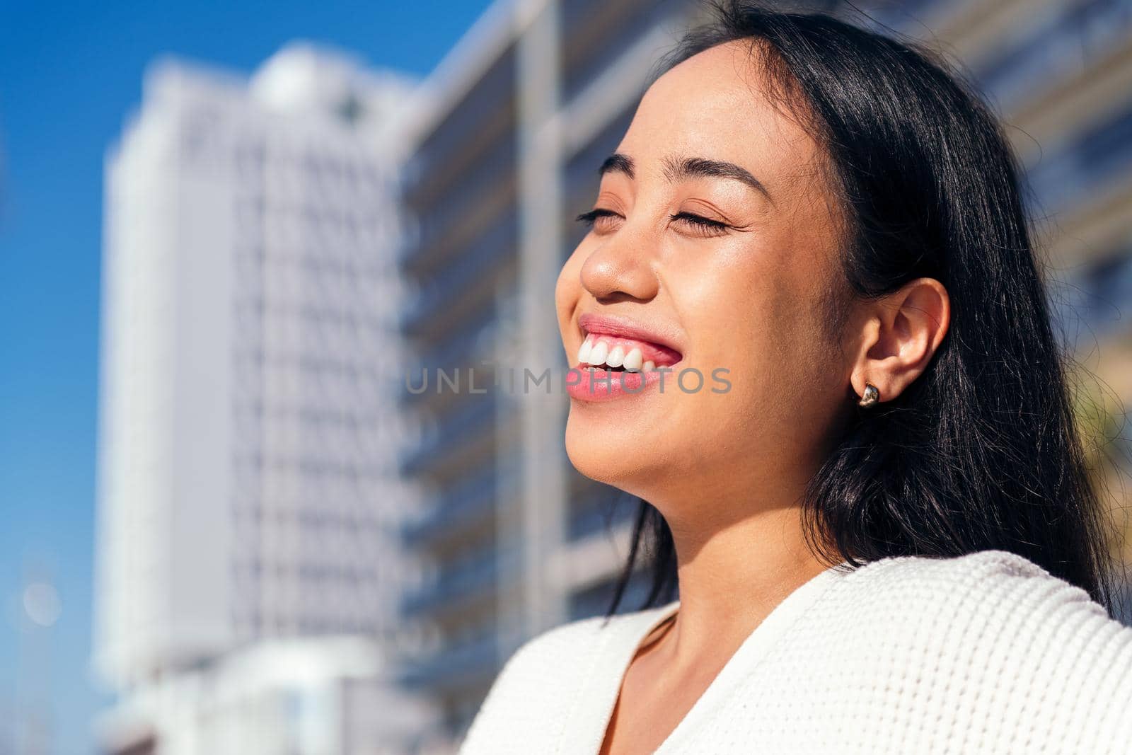 happy young asian woman smiling outdoors at city with the sun shining on her face