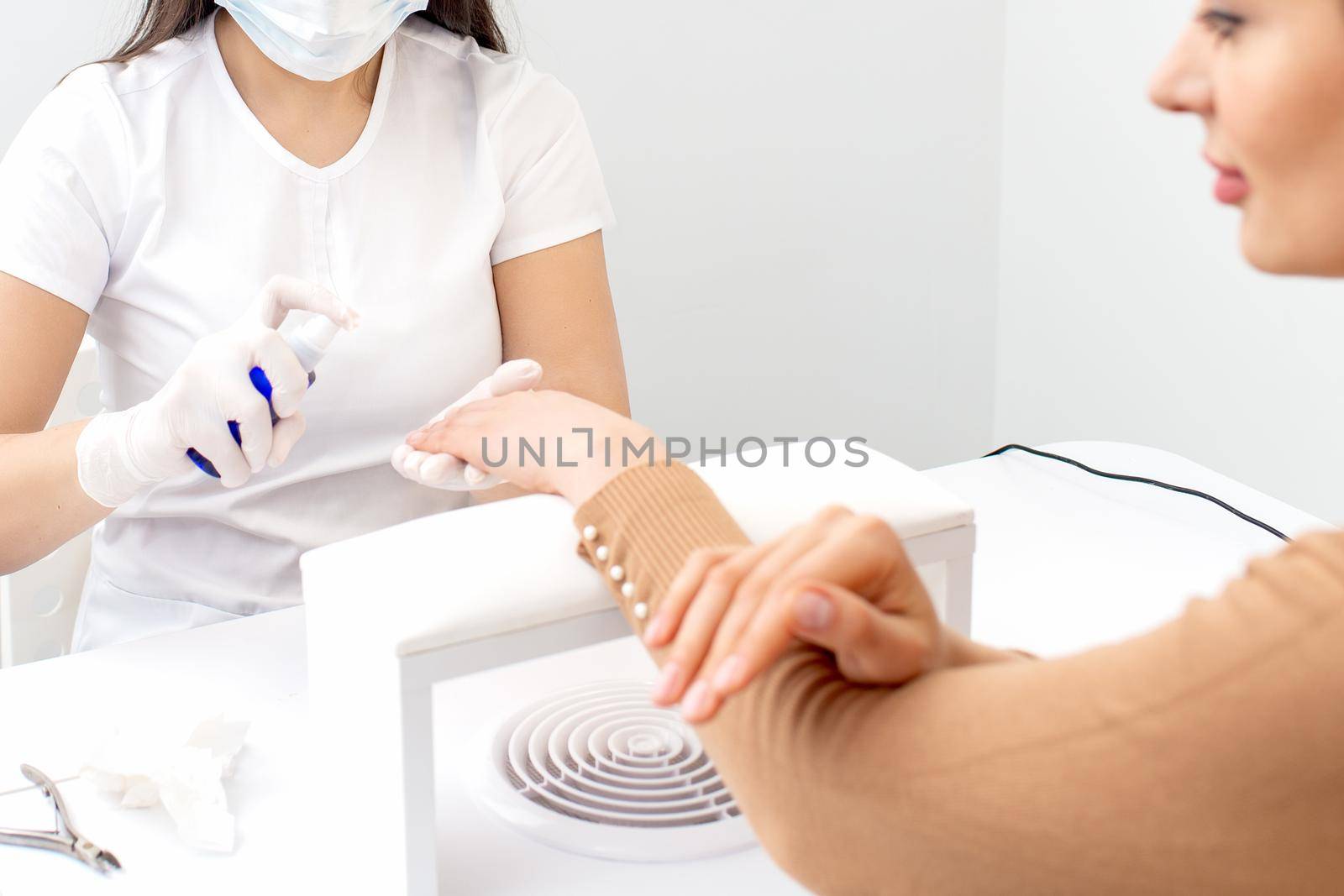 Manicure master is disinfecting fingers of woman with spray in manicure salon.